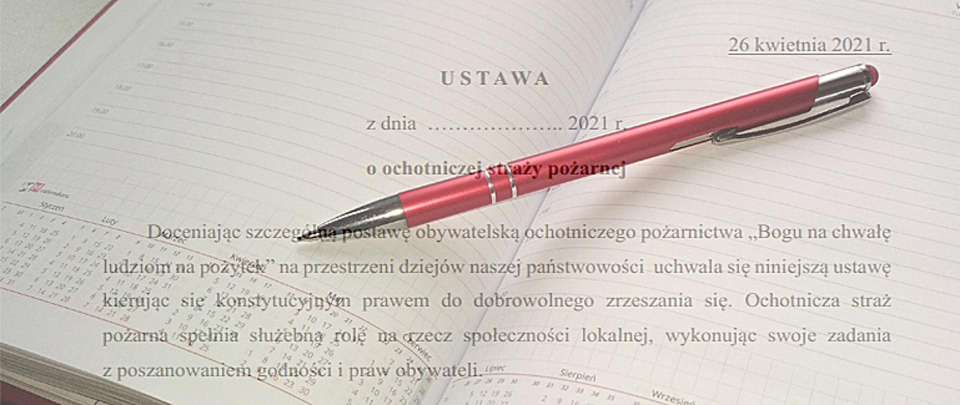 Zdjęcie przedstawia otwarty kalendarz w postaci książki, na środku otwartego kalendarza leży długopis barwy czerwonej, na dole strony widać skrócony kalendarz w postaci tabeli na cały rok, na pierwszym planie znajduje się projekt ustawy o ochotniczych strażach pożarnych.
