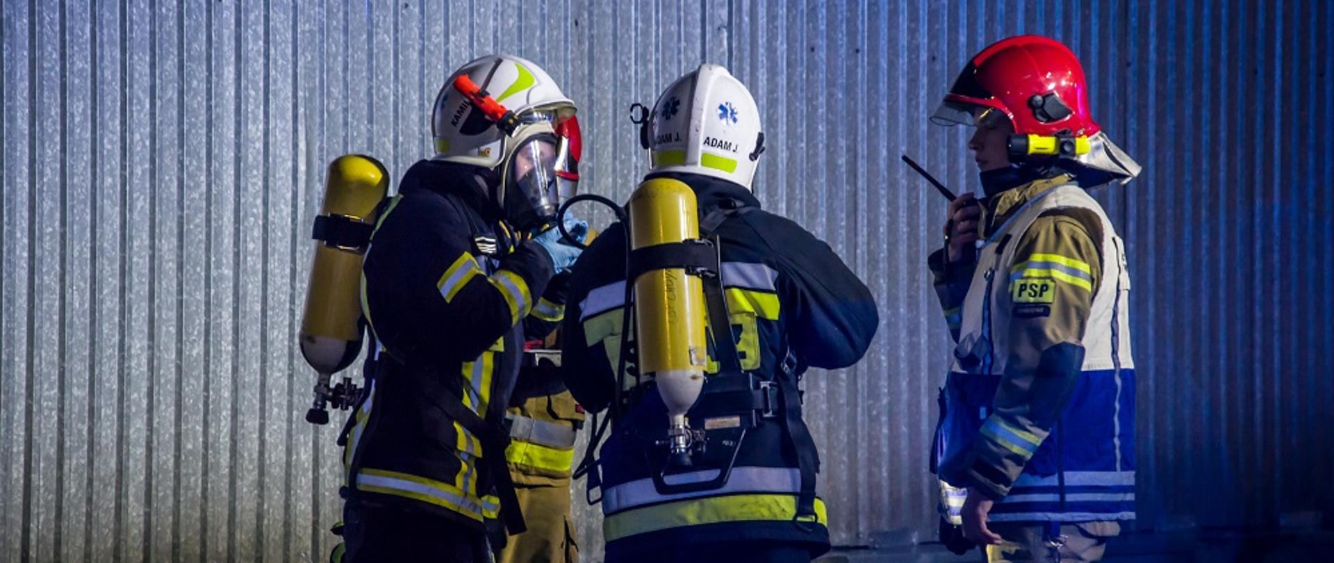 Zdjęcie przedstawia strażaków uczestniczących w ćwiczeniach na terenie JRG i zakładu produkującego akumulatory.
W tle budynki.
