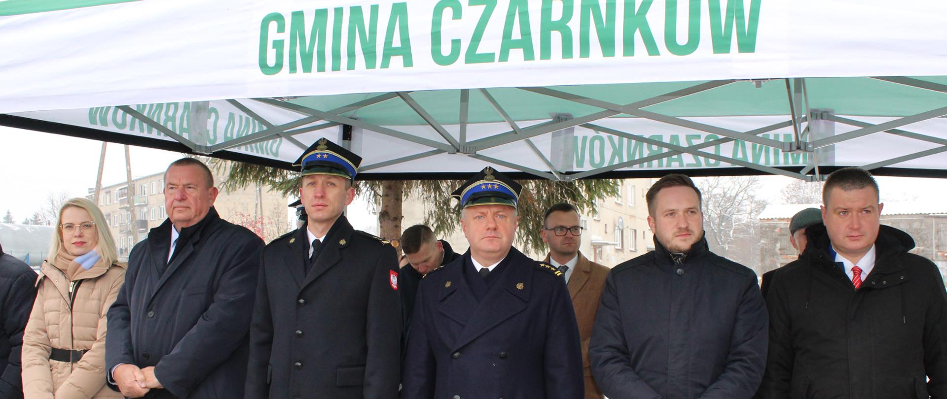 grupa ludzi w tym strażacy stoją pod biało zielonym namiotem z napisem gmina czarnków.