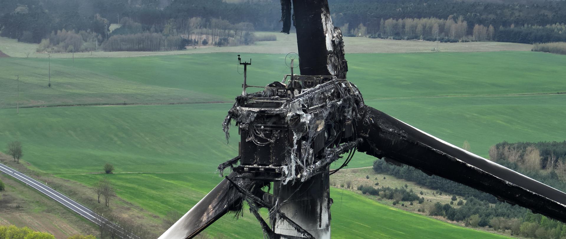 Widok spalonej gondoli turbiny wiatrowej oraz nadpalonych łopat wirnika.