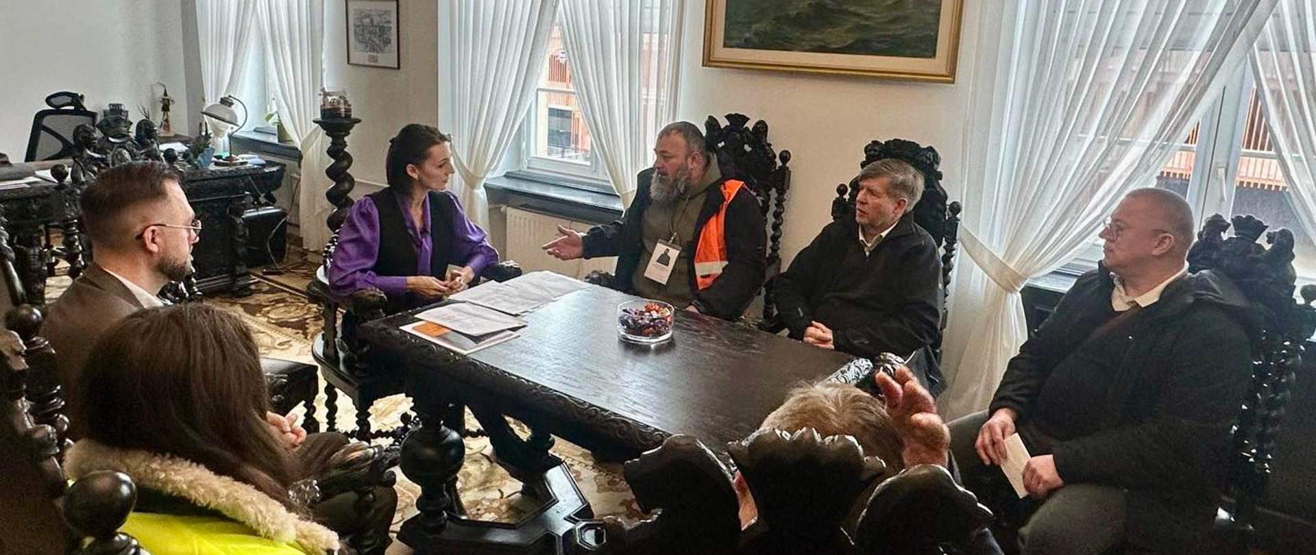 Grupa osób siedzi przy stole i rozmawia