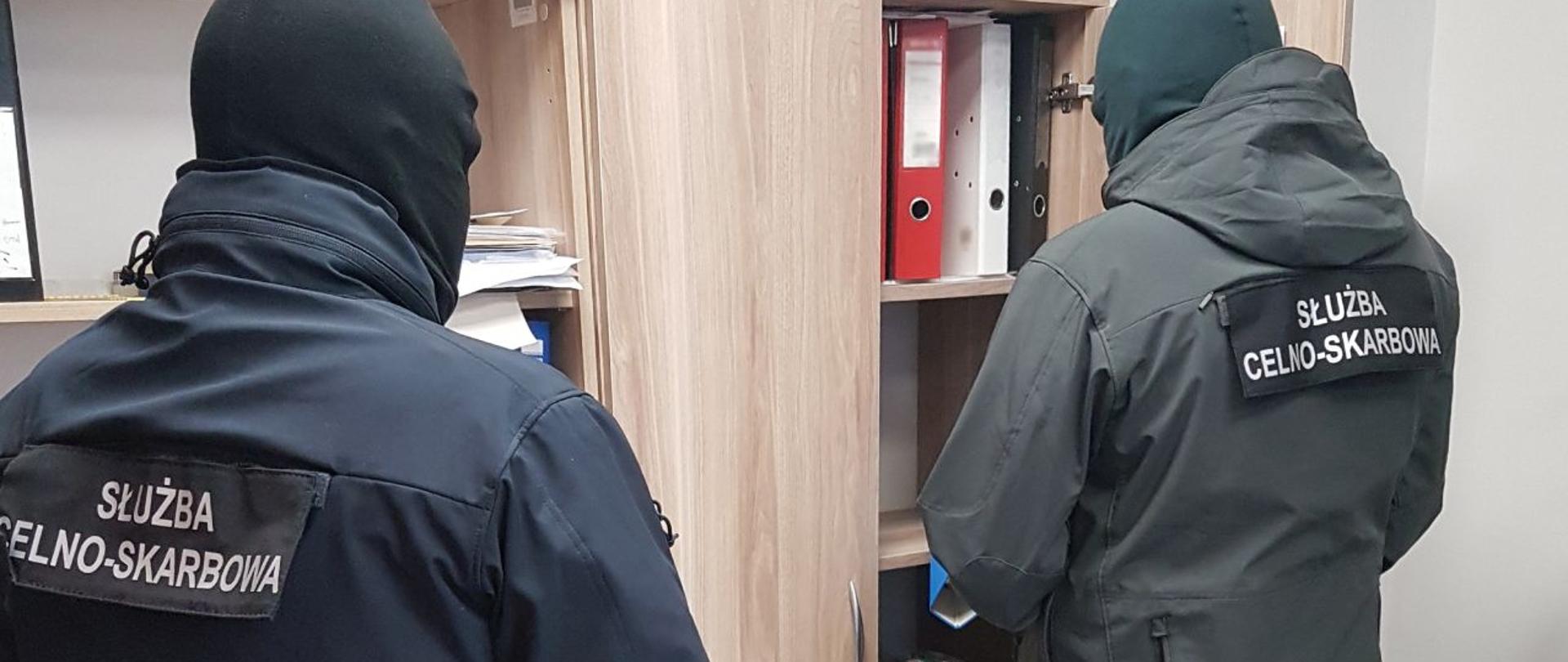 Funkcjonariusze KAS przy otwartej szafie, podczas sprawdzania dokumentów.