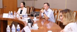 Przy stole siedzi trójka z powołanych konsultantów medycznych. Patrzą na wprost. Słuchają co mówi osoba siedząca na przeciwko. 