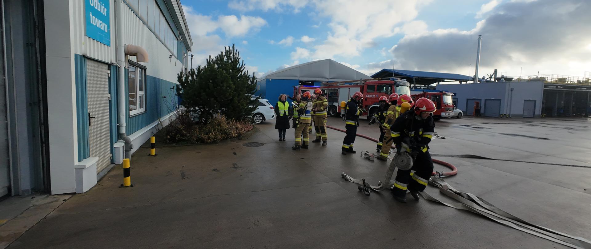 Na zdjęciu widać strażaków na początku działań. Rozwijanie linii wężowych oraz przygotowanie strażaków do wejścia do wnętrza obiektu. 