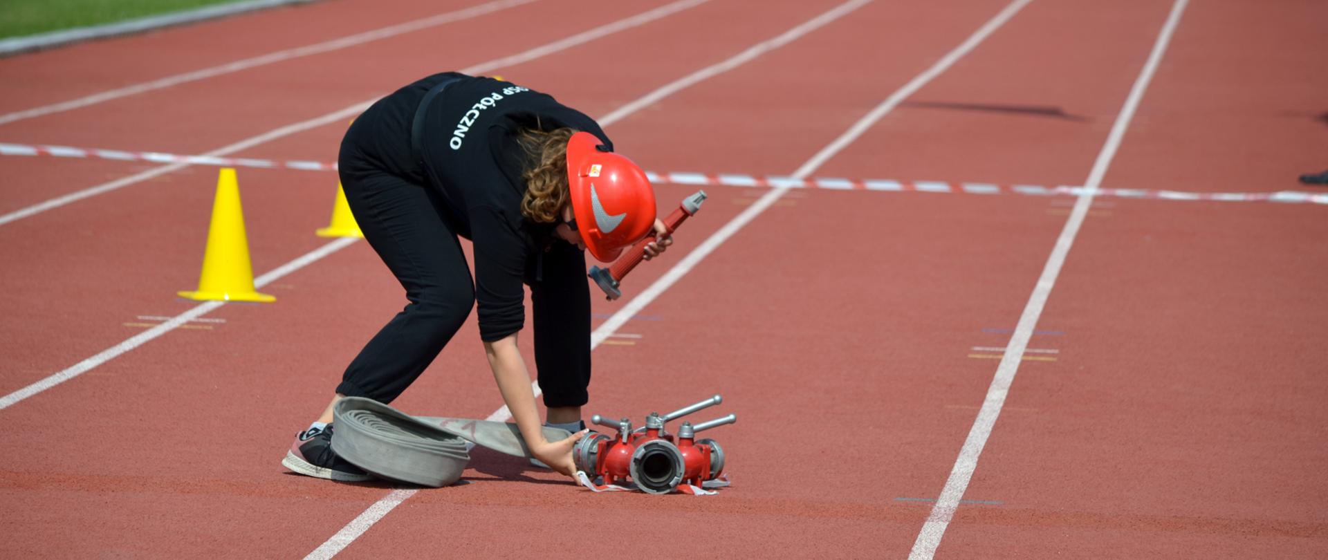 Na zdjęciu widać uczestnika zawodów podczas jednej z konkurencji podłączajacego wąż do rozdzielacza