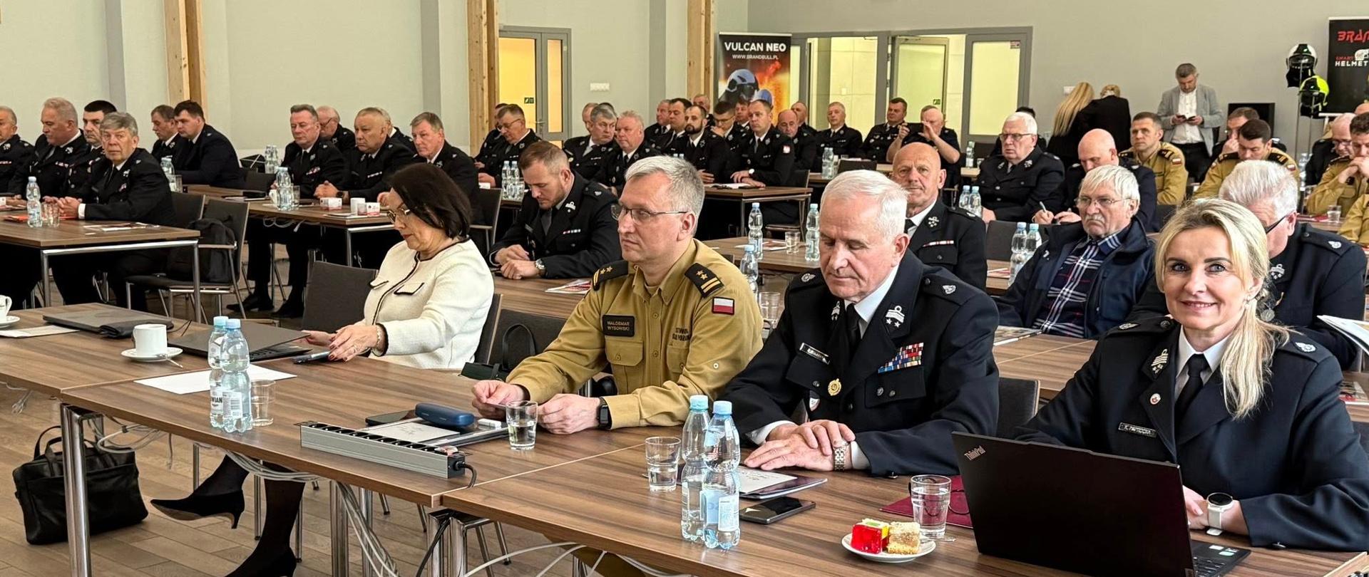 Zastępca Mazowieckiego Komendanta Wojewódzkiego bryg. Waldemar Wysowski oraz inni siedzą przy stołach. 
