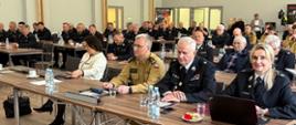 Zastępca Mazowieckiego Komendanta Wojewódzkiego bryg. Waldemar Wysowski oraz inni siedzą przy stołach. 