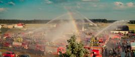 Na zdjęciu samochody pożarnicze ustawione na boisku podczas FIRE TRUCK SHOWER. Z samochodów pożarniczych podawana jest woda z działek.