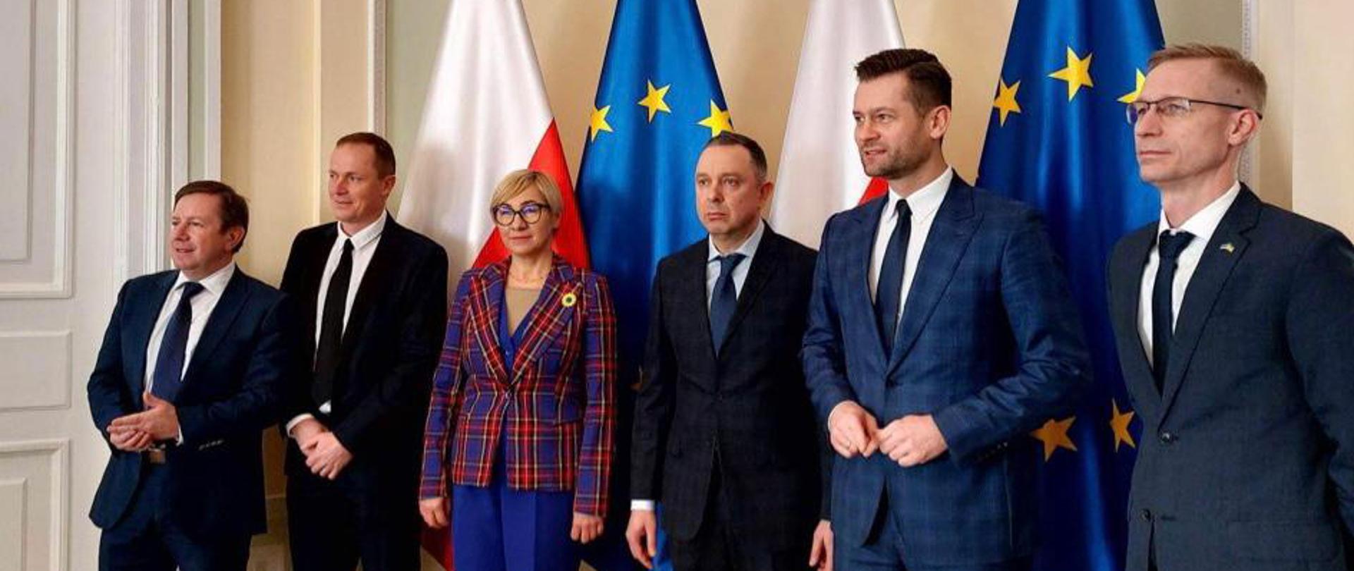 Na zdjęciu znajduje się sześcioro elegancko ubranych osób. Osoby te pozują na tle flag Polski i Unii Europejskiej.