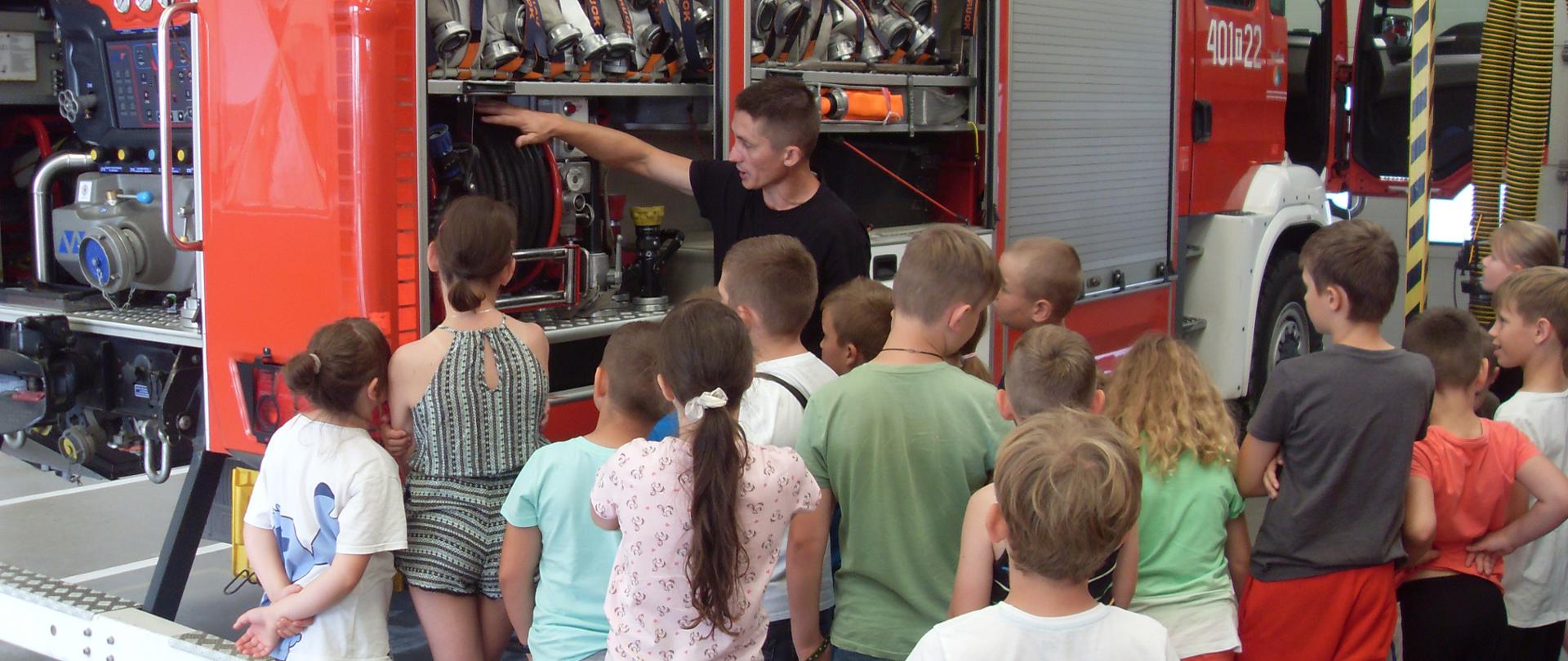 Zdjęcie przedstawia dzieci w garażu straży podczas pokazu sprzętu.