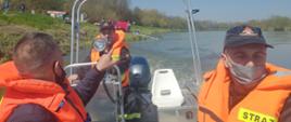Zdjęcie przedstawia strażaków płynących łodzią, którzy przeszukują obszar wodny na rzece Wisła 