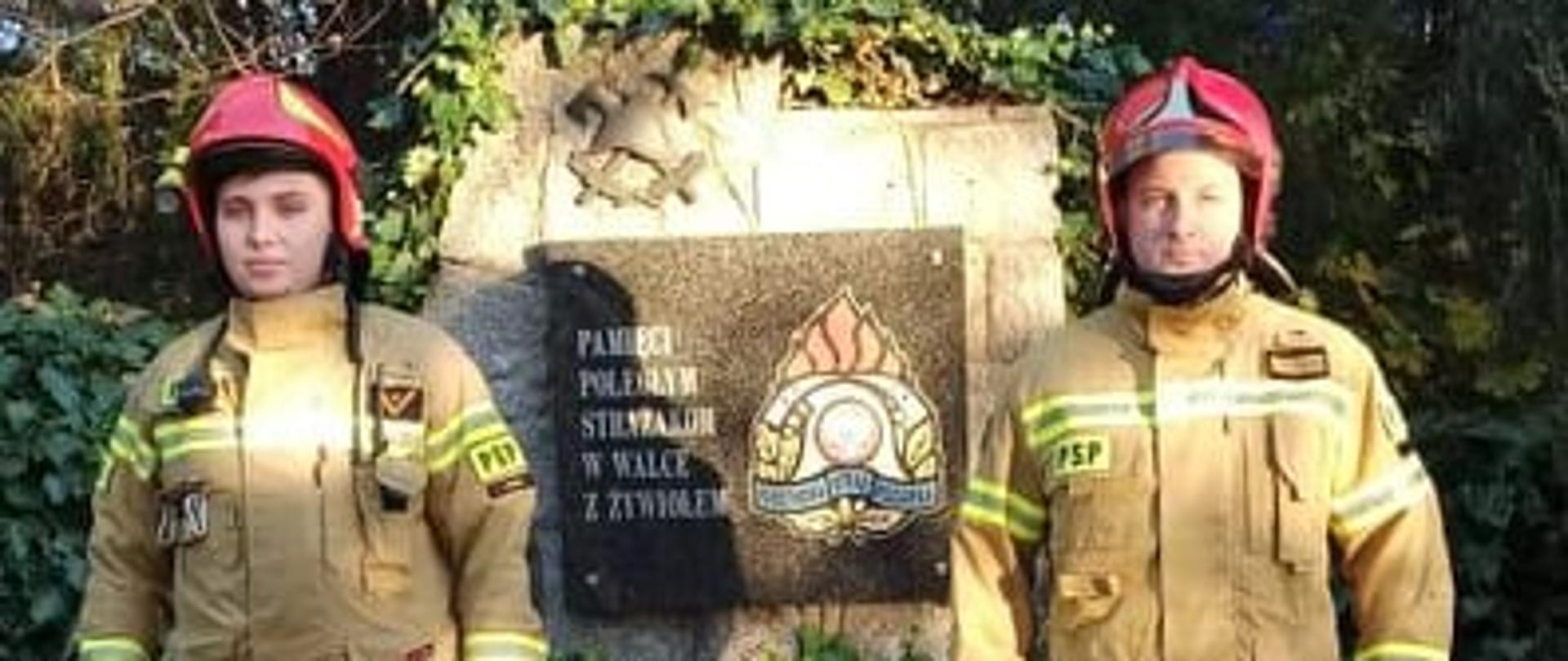 Zdjęcie przedstawia strażaków stojących przy stacji poświęconej zmarłym strażakom w celu uczczenia ich pamięci. 