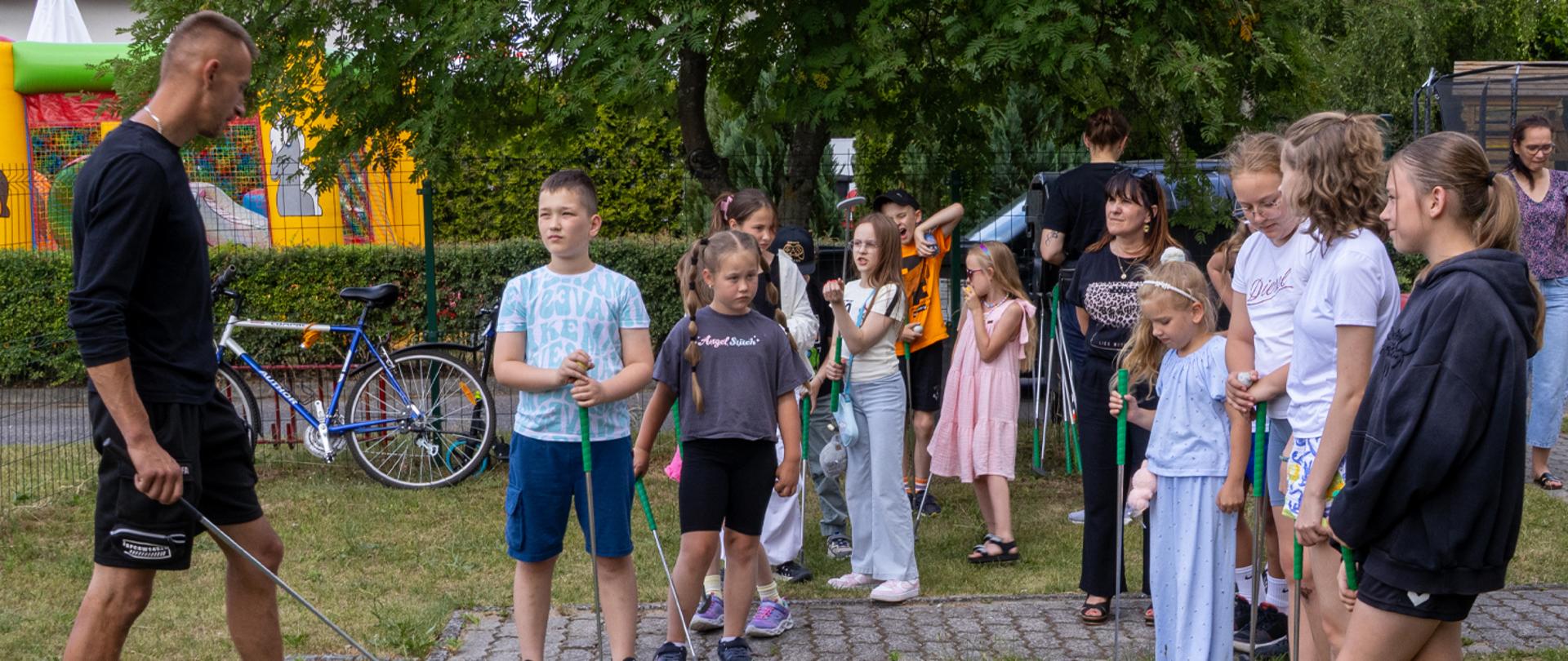 Na zdjęciu grupa osób - dzieci i dorosłych słucha instruktora gry w golfa.