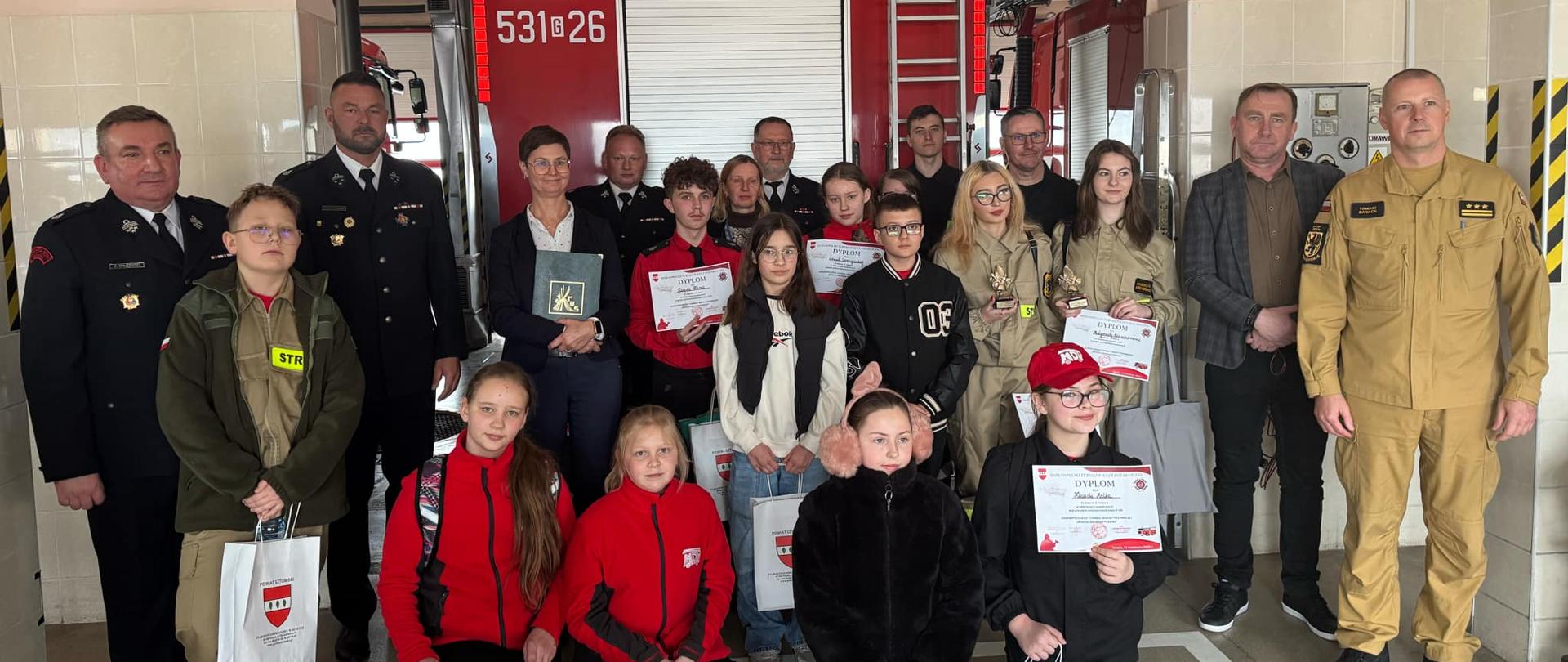 uczestnicy konkursu wraz z organizatorami stoją na garażu JRG