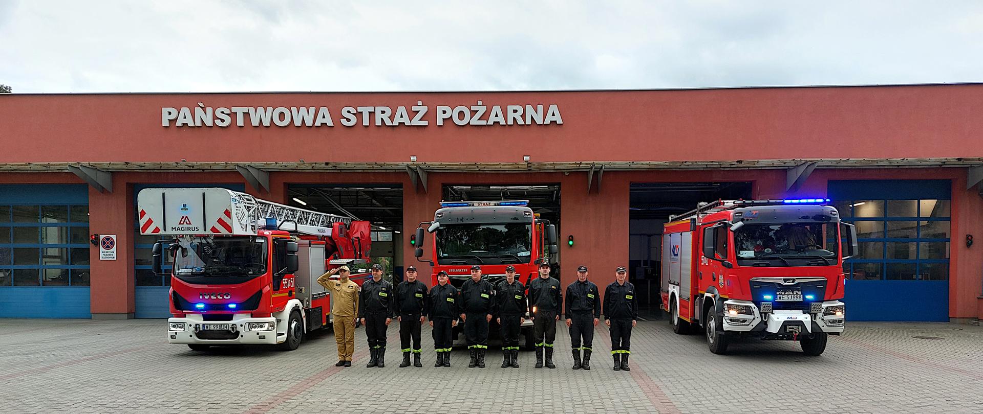 Strażacy z KP PSP Otwock na tle pojazdów i budynku komendy oddają hołd uczestnikom powstania warszawskiego