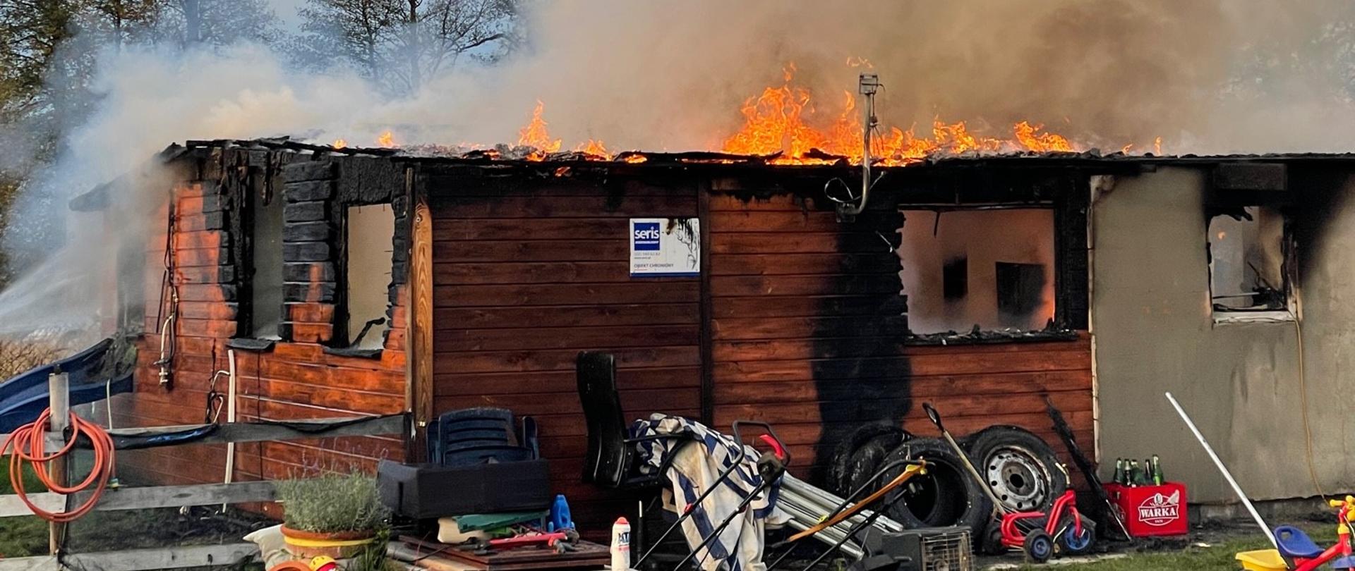 Pali się drewniano-murowany domek letniskowy. Widoczne ogień na dachu i zadymienie wewnątrz.