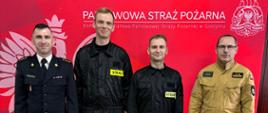 Komendanta wraz z zastępcą oraz dwóch nowych strażaków którzy stoją przed banerem gostyńskiej komendy i pozują do zdjęcia. Nowi strażacy stoją w środku a komendanci po bokach. Komendant ubrany jest w umundurowanie wyjściowe. Zastępca w umundurowanie służbowe koloru piaskowego. Nowi strażacy w umundurowanie koszarowe.