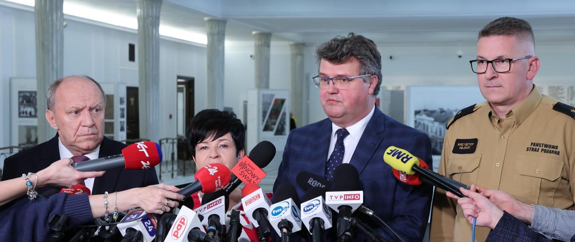 Przedstawiciele parlamentu (2 osoby) wiceminister MSWiA oraz z-ca KG PSP stoją przy mikrofonach podczas konferencji prasowej