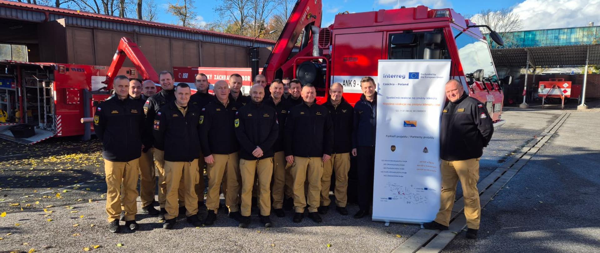 Zdjęcie grupowe funkcjonariuszy uczestniczących w wymianie dowódców na szkoleniu w Czechach w tle pojazd ratowniczy.