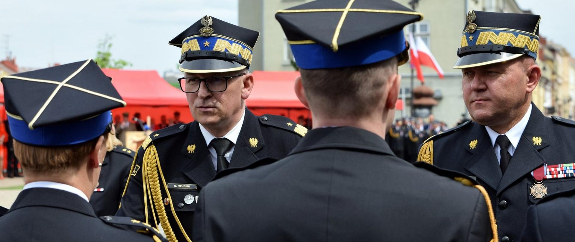 Zdjęcie zrobione na zewnątrz. Strażacy ustawieni w szeregu na zbiórce otrzymują odznaczenia. 