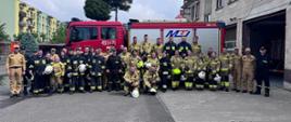 Zdjęcie grupowe po zakończonym egzaminie. Słuchacze oraz egzaminujący stoją na tle samochodu pożarniczego. 