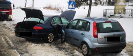 Widać dwa samochody, które zderzyły się ze sobą, znajdują się na drodze