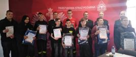 Grupa laureatów turnieju wraz komendantem i komisją sędziowską na tle loga Państwowej Straży Pożarnej 