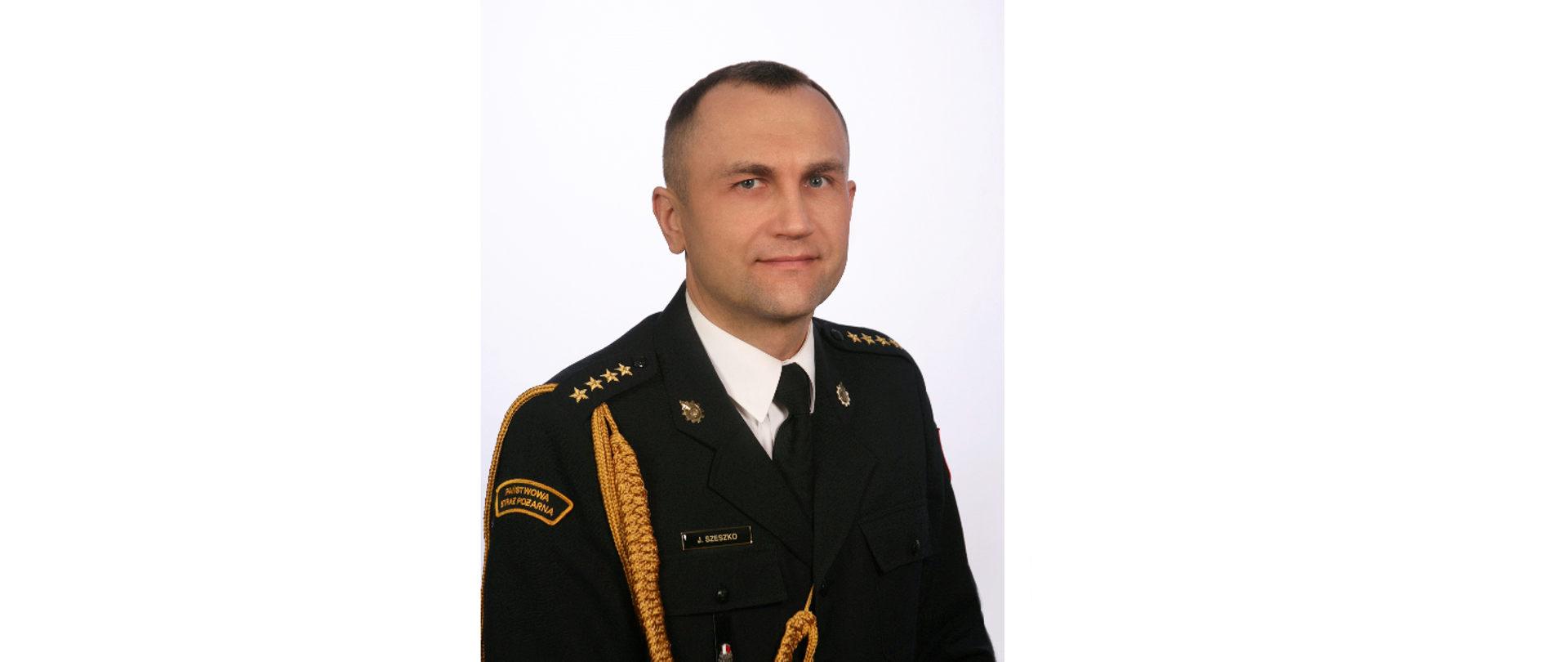 Zdjęcie portretowe st. kpt. Jarosława Szeszko Komendanta Powiatowego Państwowej Straży Pożarnej w Grajewie w mundurze wyjściowym na jasnym tle.