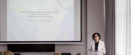 Sala konferencyjna, kobieta stoi za mównicą z polską flagą, z tyłu na ekranie widnieje napis: "Polityka RP wobec krajów Globalnego Południa (Afryka, Bliski Wschód) oraz polska pomoc rozwojowa