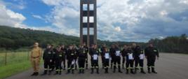 Na zdjęciu grupa strażaków OSP w ubraniach koszarowych stoją w dwuszeregu w rękach trzymają zaświadczenie ukończenia kursu. Obok stoi umundurowany funkcjonariusz KP PSP. W tle wspinalnia oraz las.