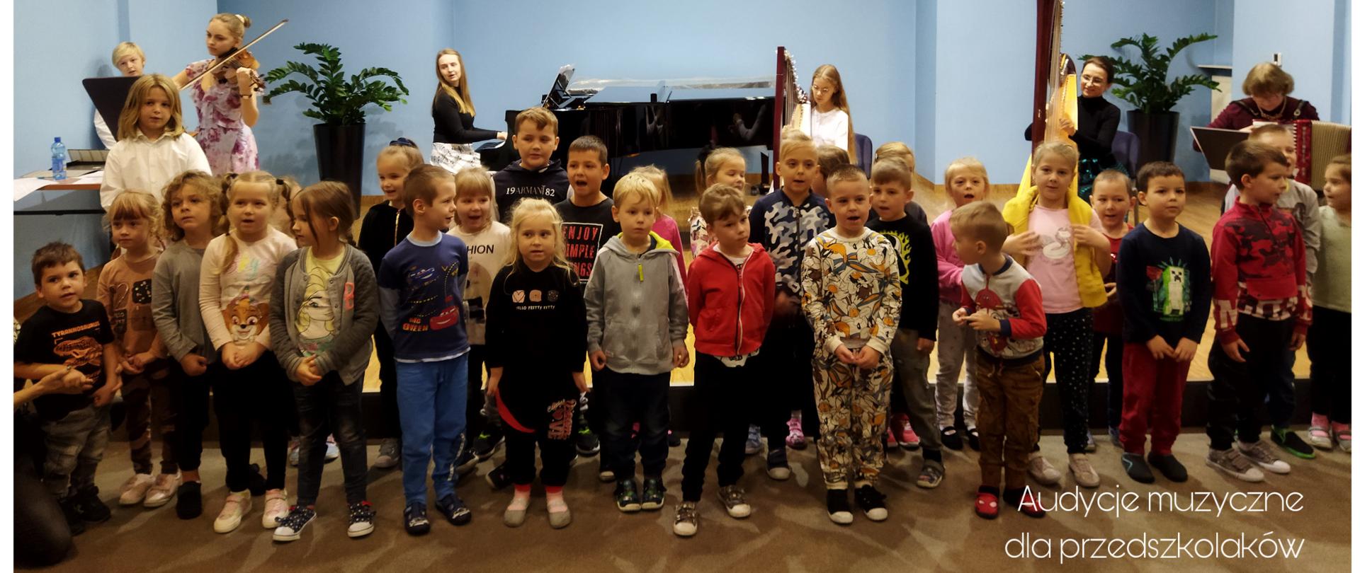Kolaż składający się z 7 kolorowych zdjęcie z audycji muzycznych odbywających się w naszej szkole. Cztery zdjęcia przedstawiają osoby znajdujące się na scenie w sali kameralnej i grające na poszczególnych instrumentach: harfy, klarnet, akordeon i fortepian, jedno zdjęcia przedstawiają dzieci zgromadzone w sali perkusyjnej słuchające grającego na ksylofonie ucznia a drugie w sali organowej słuchające opowieści na temat organów, ostatnie zdjęcie to zdjęcie grupowe przedstawiające grupkę dzieci stojących przed samą sceną i śpiewających piosenkę oraz grupę muzyków występujących wspólnie z dziećmi i grających na skrzypcach, fortepianie, 2 harfach i akordeonie.