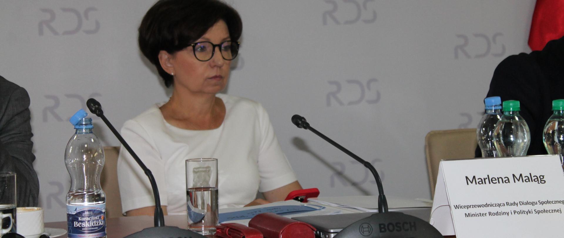 Na zdjęciu za stołem prezydialnym siedzi Marlena Maląg - Minister Rodziny i Polityki Społecznej. W tle baner z napisem Rada Dialogu Społecznego