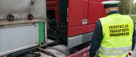 Od lewej: umundurowany inspektor warmińsko-mazurskiej ITD stoi obok zatrzymanego do kontroli ciągnika siodłowego z naczepą ciężarową.