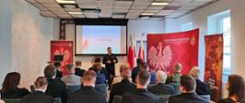Zdjęcie przedstawia Zastępce Śląskiego Komendanta Wojewódzkiego - bryg. Arkadiusza Krzemińskiego, stojącego i przemawiającego do zebranych gości na tle ekranu projekcyjnego