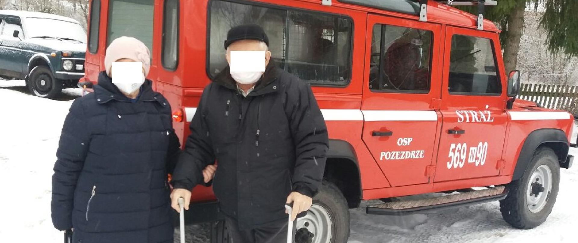 Dwie osoby starsze stoją przy samochodzie z OSP Pozezdrze. Mężczyzna ma dwie kule. 