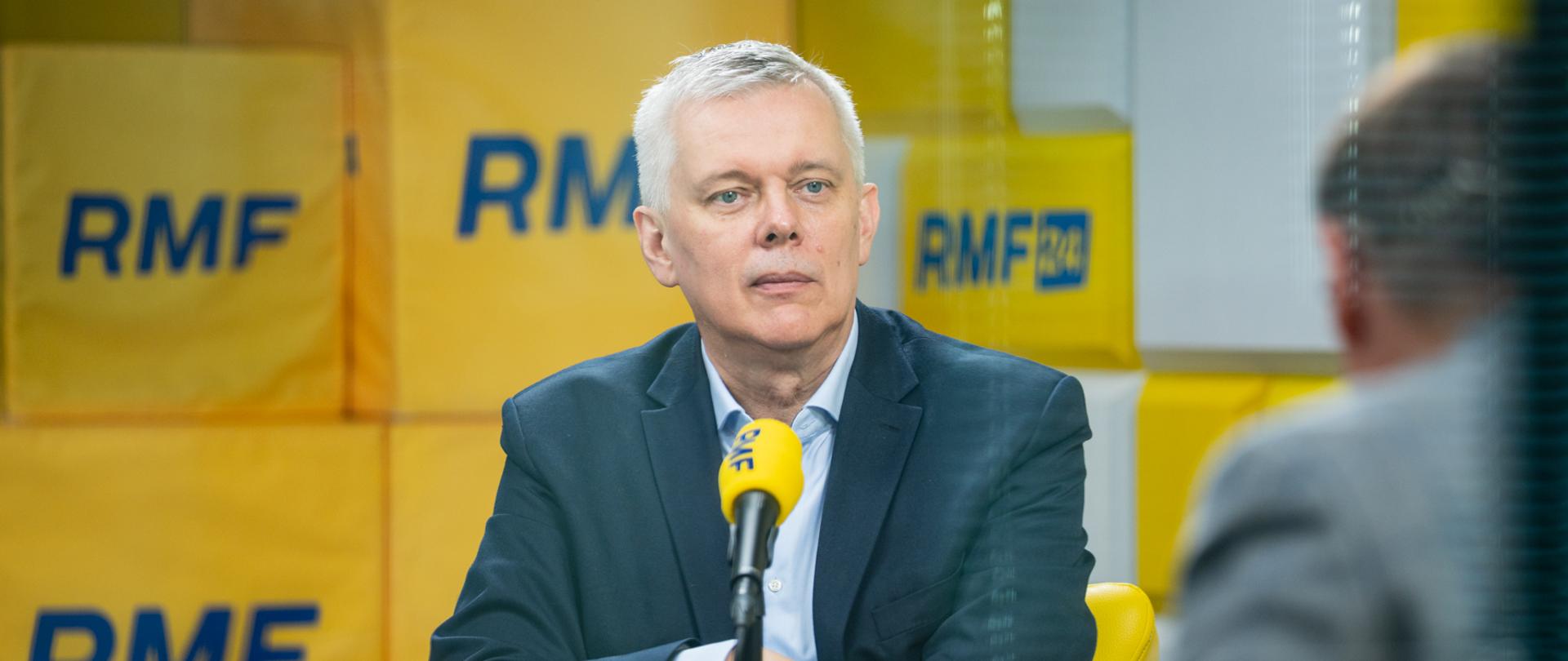 Na zdjęciu minister Tomasz Siemoniak siedzący w studiu radia RMF FM przed żółtym mikrofonem z niebieskim napisem RMF. Po prawej stronie zdjęcia widać sylwetkę siedzącego tyłem do obiektywu redaktora Tomasza Terlikowskiego. W tle na ścianie żółte i białe kwadraty z niebieskimi napisami RMF.