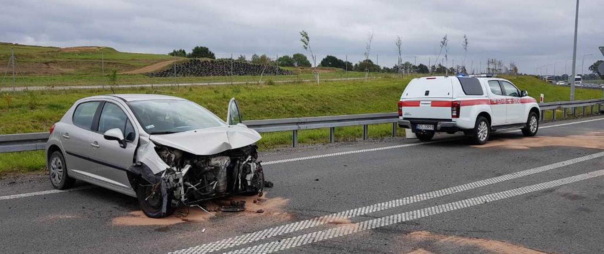 Osobowe BMW po uderzeniu w bariery energochłonne i ciężarówkę. Na drodze posypano sorbent w celu zabezpieczenia plam oleju.