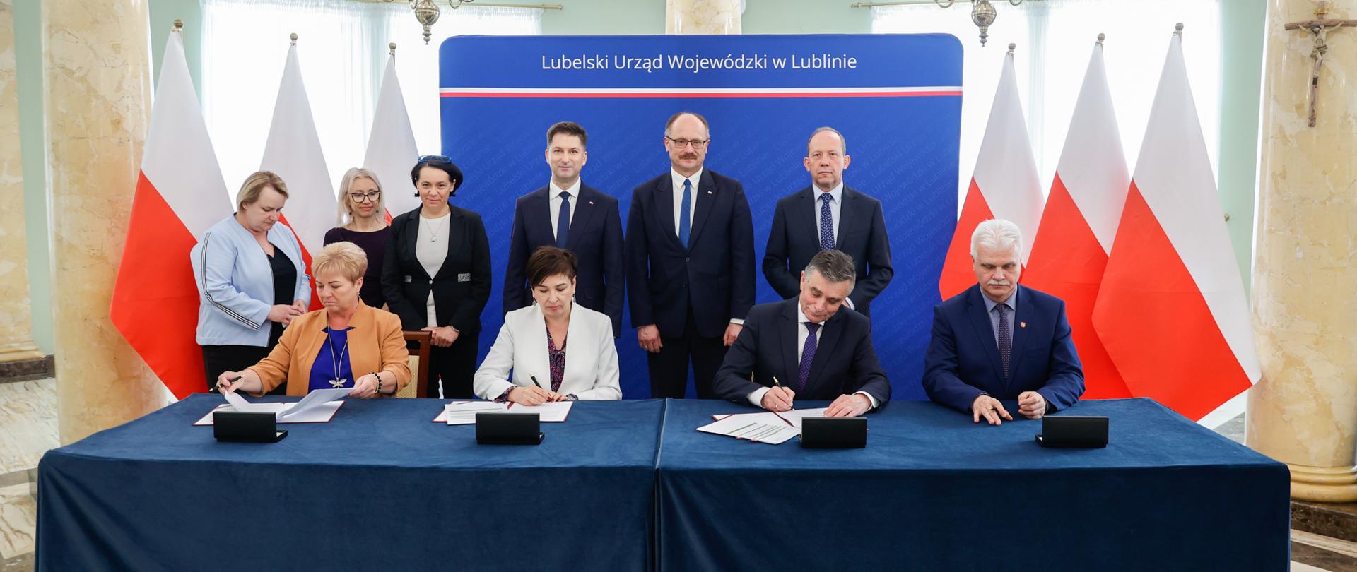 Mężczyźni i kobiety przy stole podpisują dokumenty.