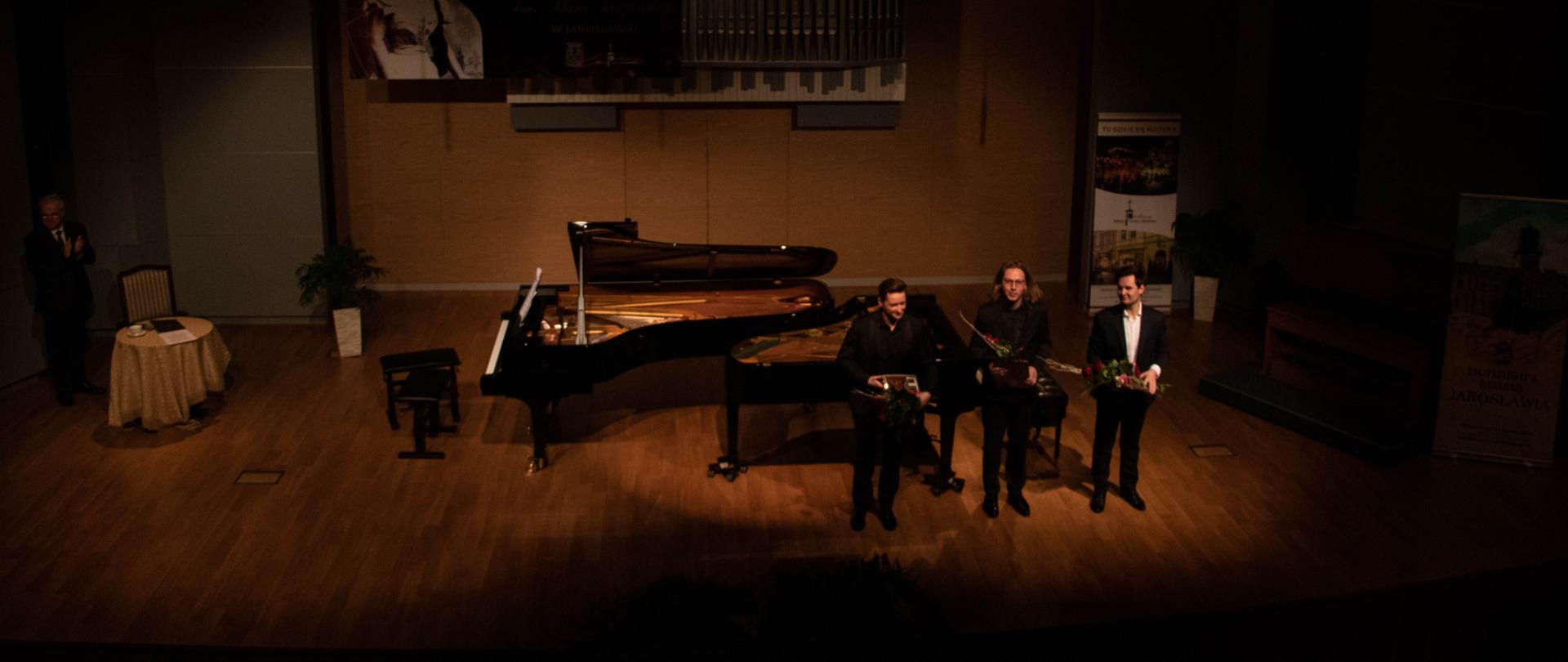 Na zdjęciu stojący na scenie obok fortepianu z kwiatami w dłoniach, kłaniający się artyści (fot. Agnieszka Kamińska). 