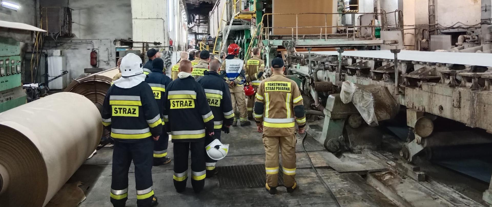 Strażacy zwiedzający halę produkcyjną w fabryce papieru.