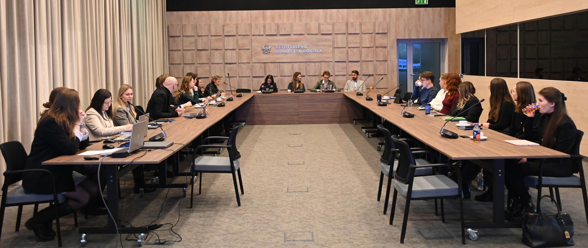 Posiedzenie Młodzieżowej Rady Klimatycznej. Osoby uczestniczące w spotkaniu siedzą za stołem ustawionym w literę U.