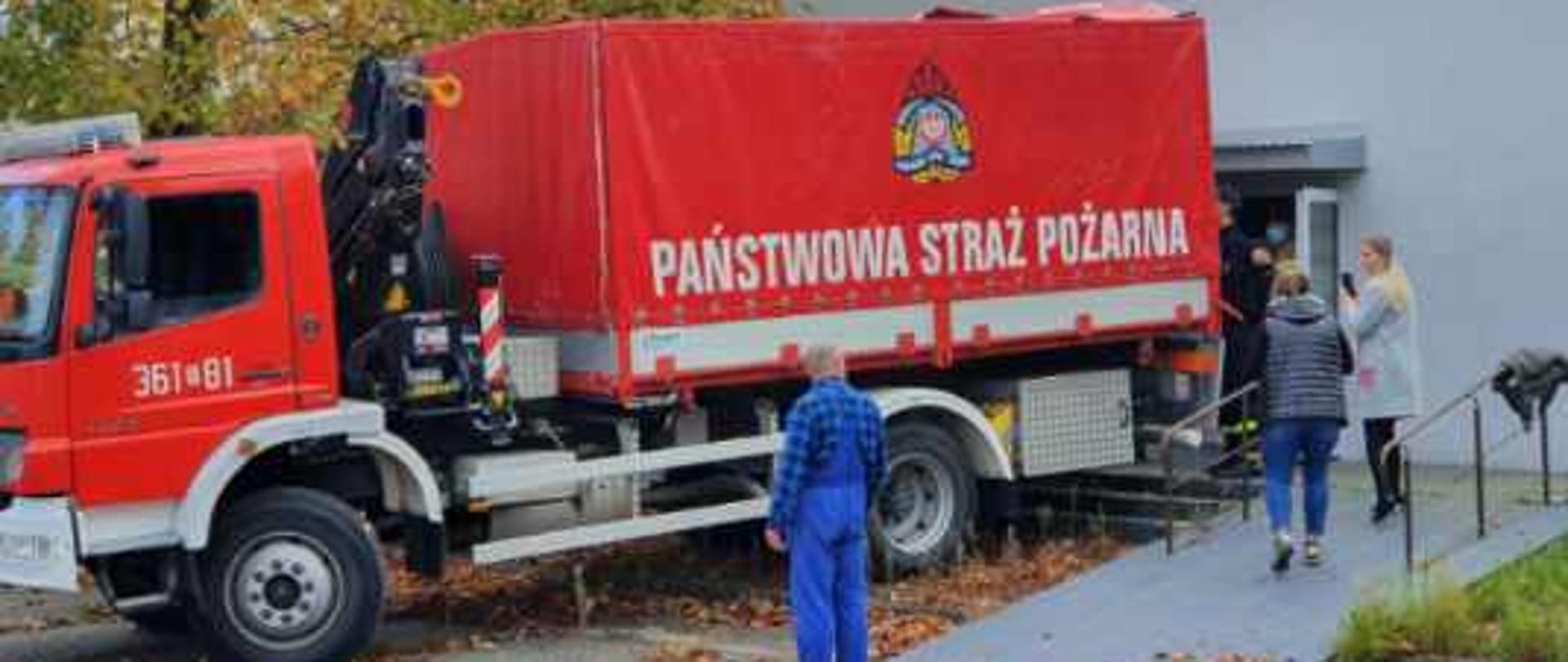 Samochód ciężarowy straży pożarnej do przewozu rzeczy pod rampą rozładunkową. Dookoła pracownicy szpitala. 