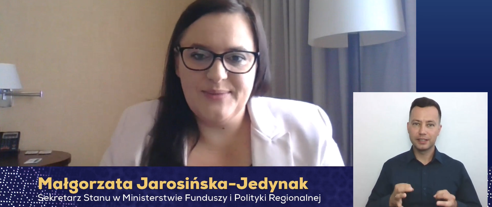Zdjęcie przedstawia Minister Funduszy i Polityki Regionalnej- Małgorzatę Jarosińską-Jedynak wypowiadającą się do kamery, ubraną w białą marynarkę. W prawym dolnym rogu widać mężczyznę tłumaczącego wypowiedź na język migowy. 