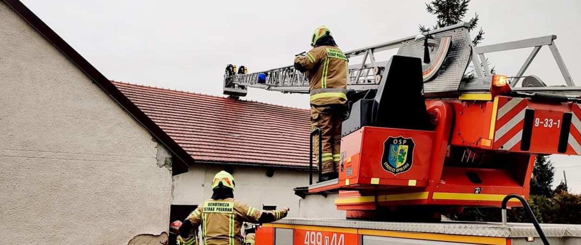 Zdjęcie przedstawia samochody pożarnicze i strażaków na tle budynków mieszkalnych