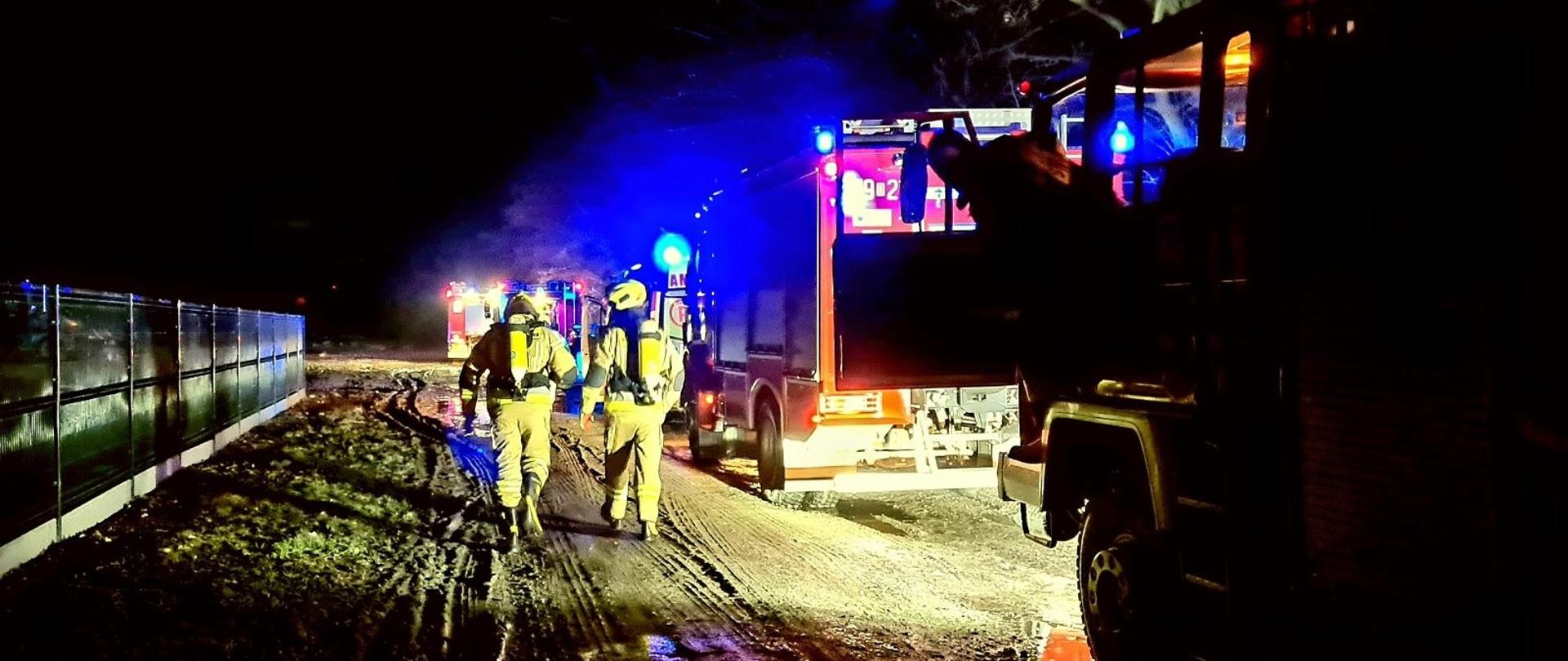 Dwaj strażacy na tle samochodów strażackich