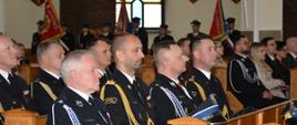 Na zdjęciu widać strażaków siedzących w drewnianej ławce podczas liturgii w kościele.