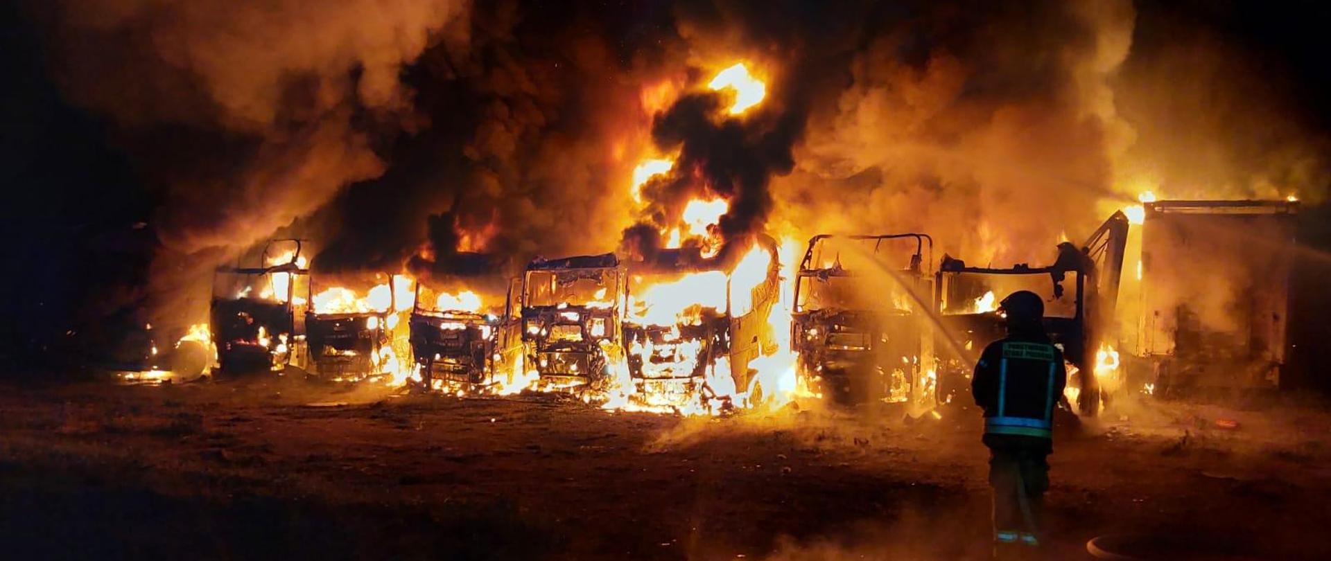 Strażak podaje prąd gaśniczy wody na palące się ciągniki siodłowe.