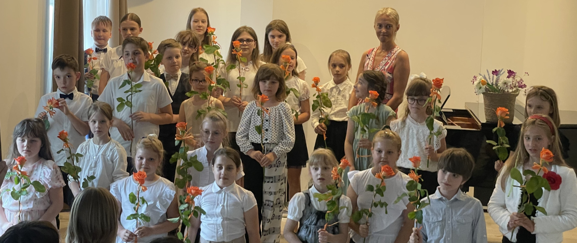 Zdjęcie dzieci, które uczestniczyły w koncercie z okazji Dnia Matki trzymające w dłoni różę dla mam. 