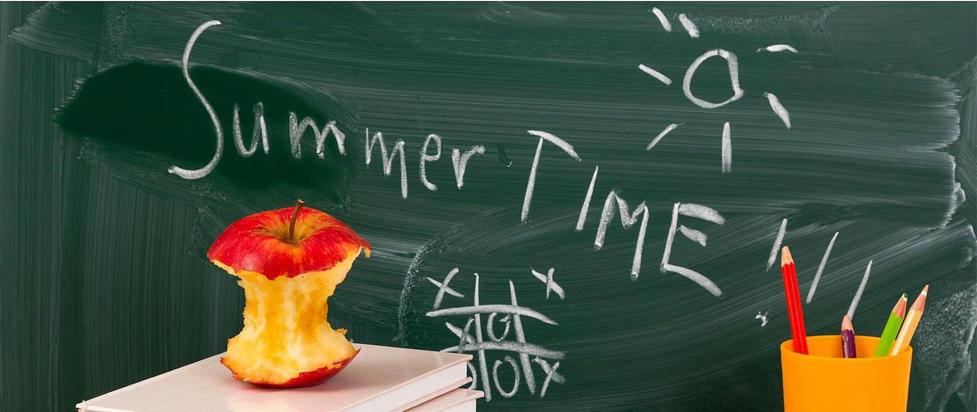 Plakat informujący o uroczystości zakończenia roku szkolnego w dniu 24 czerwca 2022 roku o godzinie 17.00. W centralnej części plakatu umieszczone jest zdjęcie przedstawiające tablicę szkolną z napisem "Summer time". Pod tablicą leżą książki, ogryzek jabłka oraz kubek z kredkami.