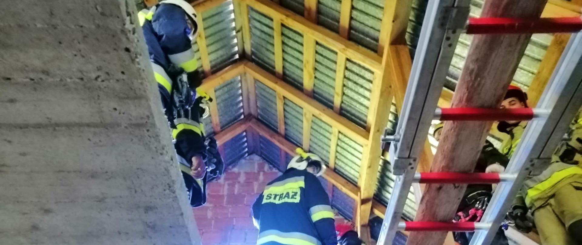Strażacy na poddaszu budynku mieszkalnego. Drabina pożarnicza leżąca na stropie budynku.